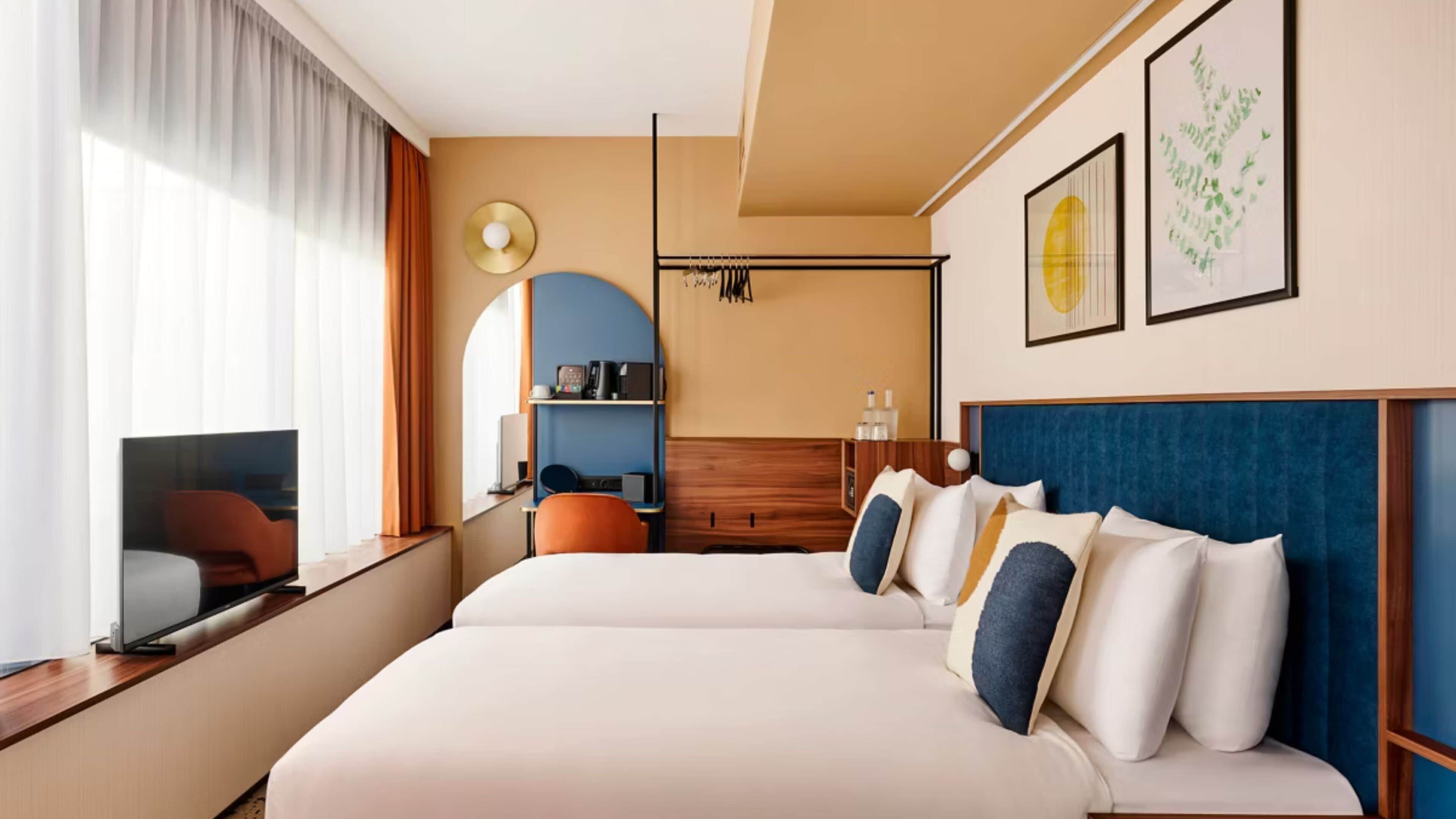 A hotel room with two beds, a TV, a desk, and a wardrobe.
