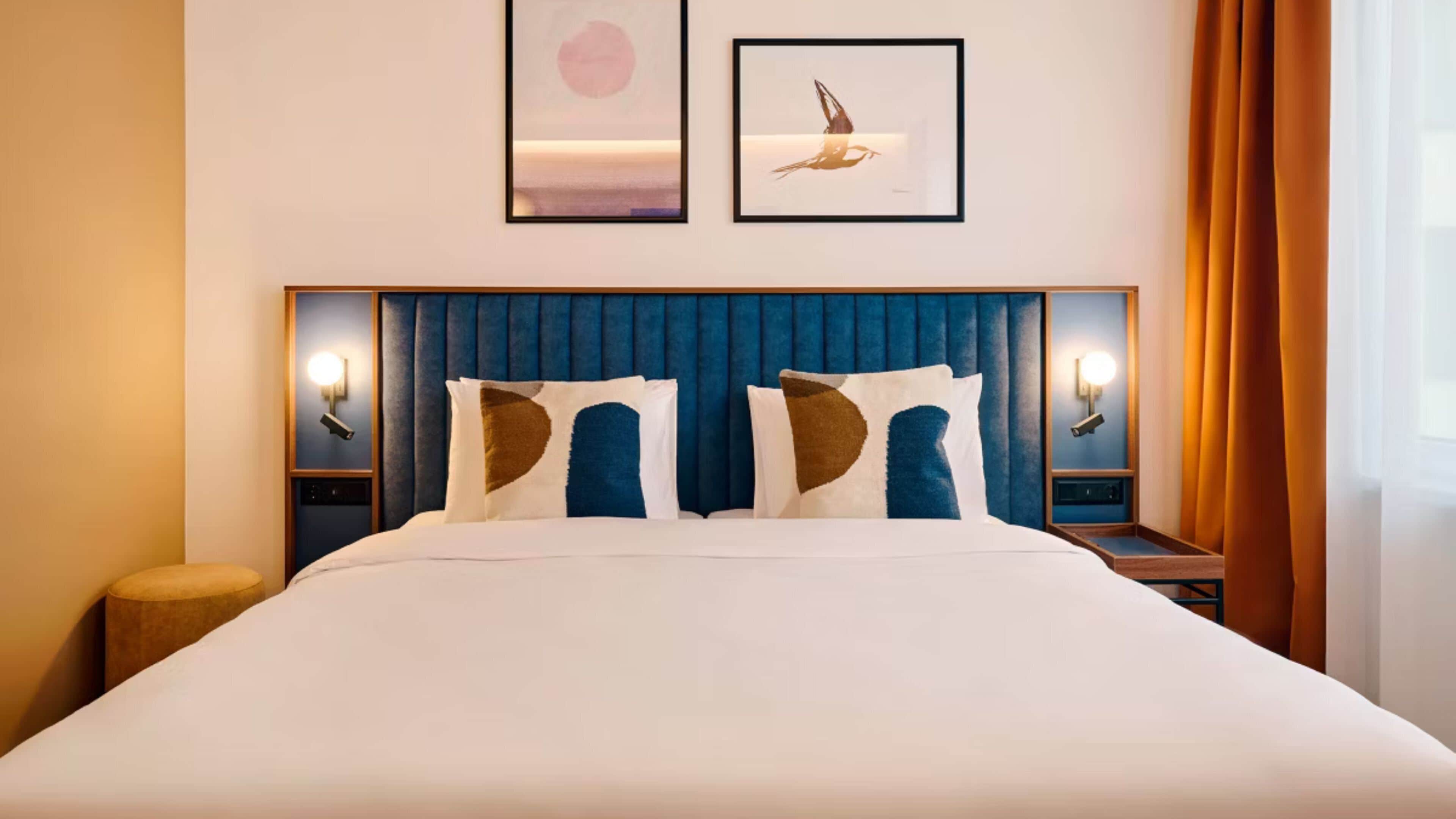 A hotel room with a large bed, two wall-mounted lamps, and two framed pictures above the bed.