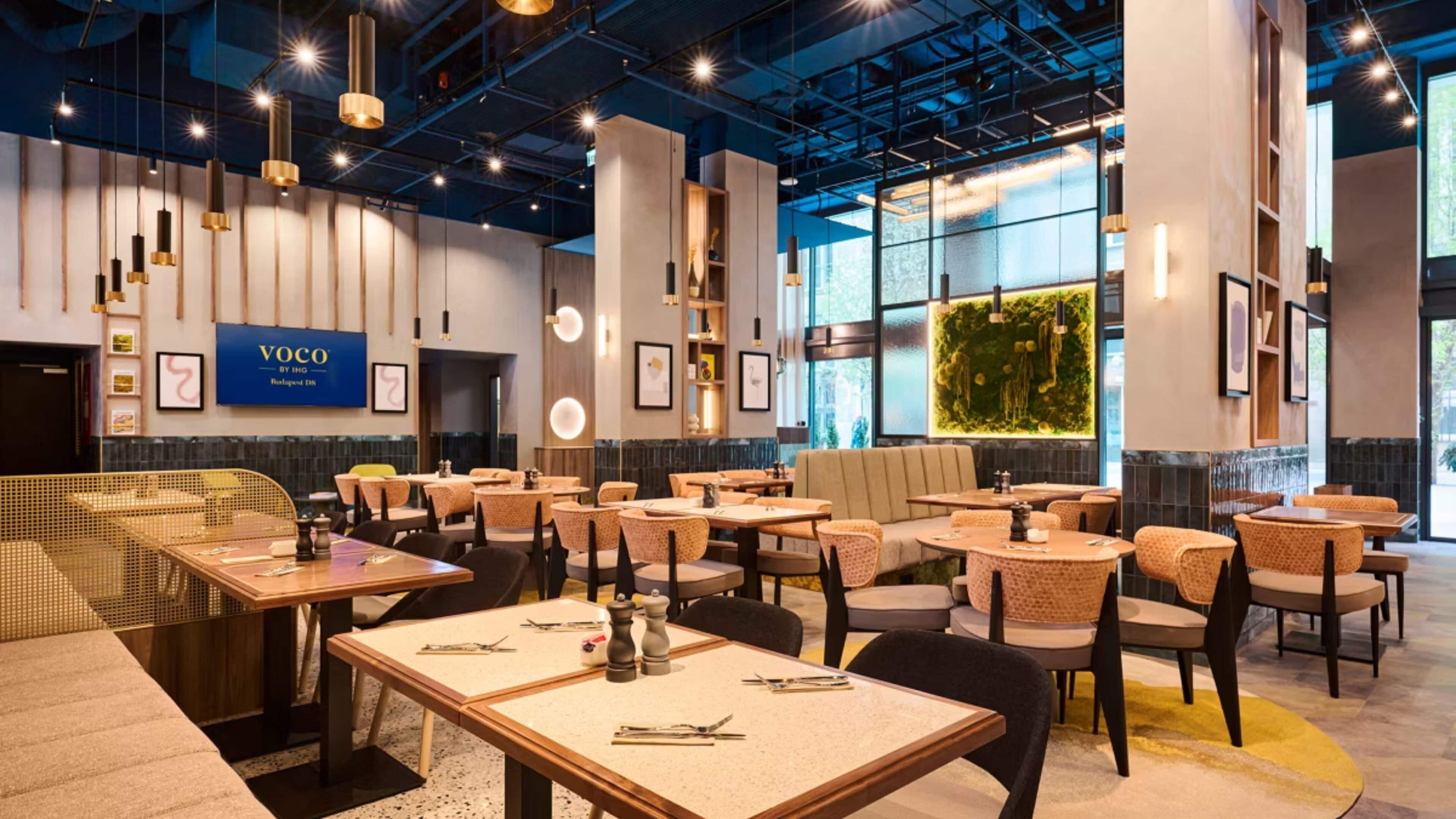 Een modern restaurantinterieur met tafels, stoelen, hangende lampen en een grote muurschildering.