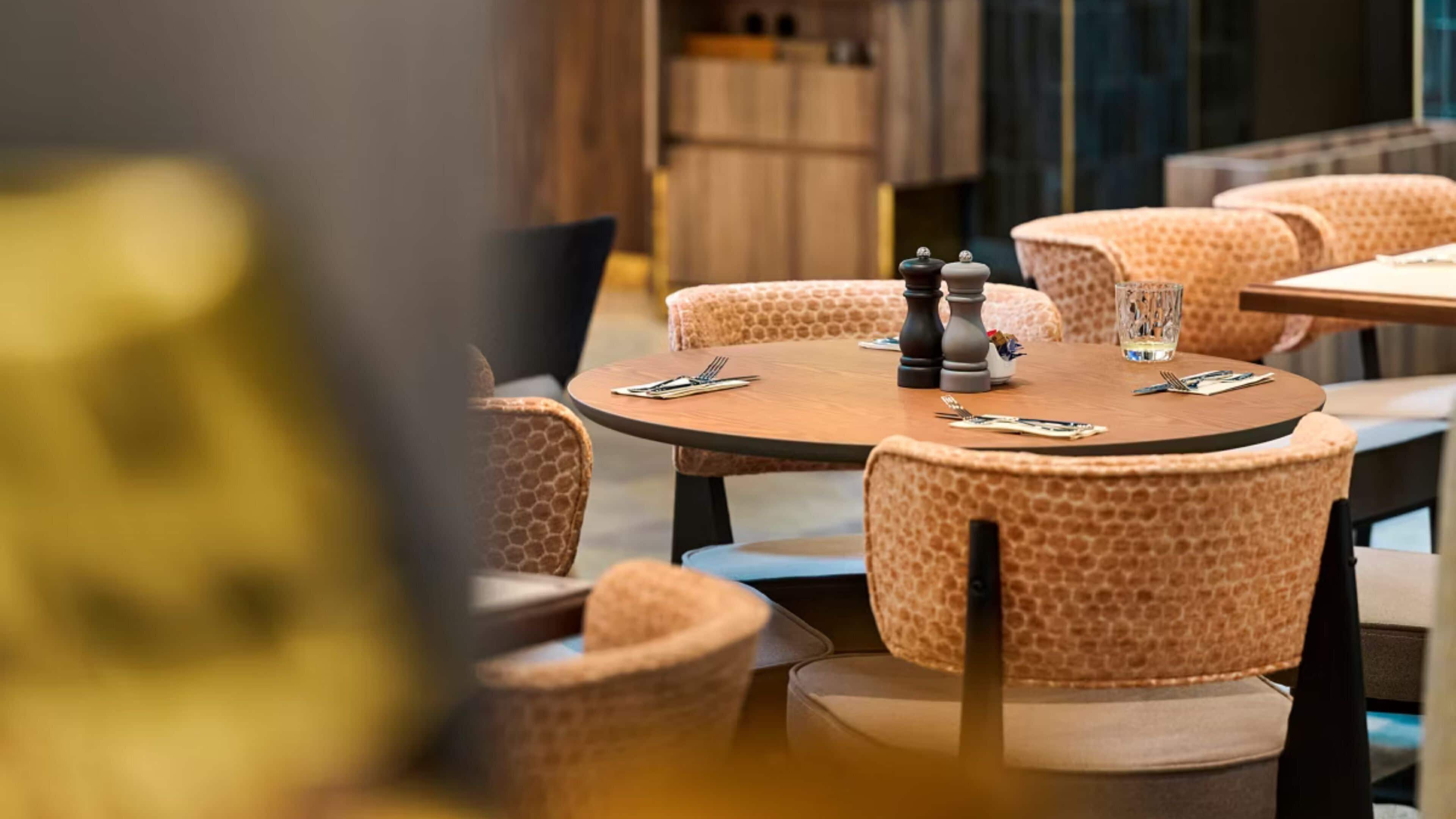 Interno di un ristorante con tavoli rotondi, sedie imbottite e set da sale e pepe su ogni tavolo.
