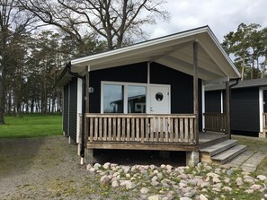 A small cabin with a wooden deck and a white door, surrounded by a gravel path and a grassy area. - Kapelludden Camping & Stugor (Borgholm)
