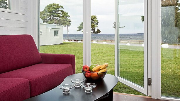 Una habitación con un sofá rojo, una mesa de vidrio con un frutero, y vista al mar a través de puertas de cristal grandes.