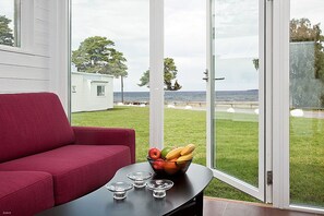 Quarto com um sofá vermelho, uma mesa de vidro com uma fruteira e vista para o mar através de grandes portas de vidro.