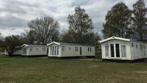 Una hilera de casas móviles con un campo de césped y árboles al fondo.