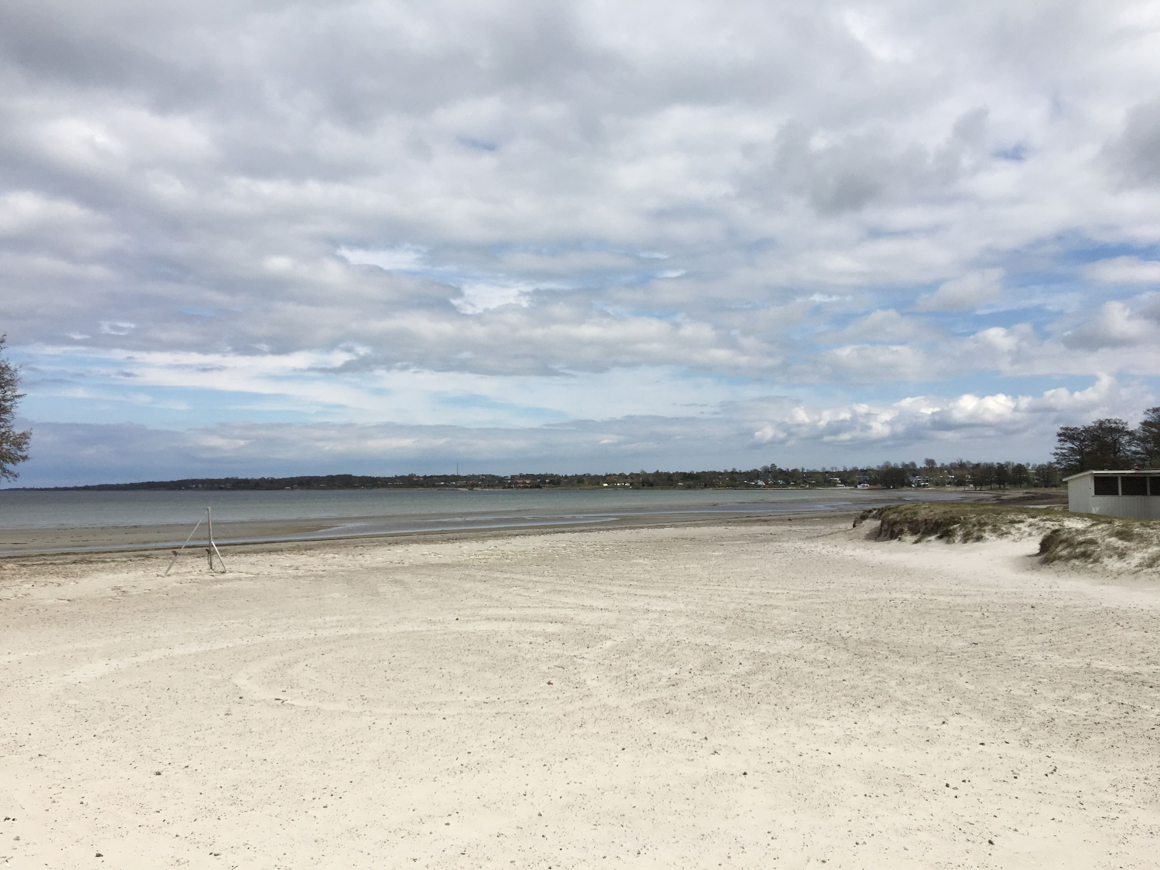 A beach with a sandy shore, a small structure on the right, and a cloudy sky.