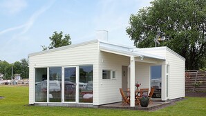 Un pequeño edificio de una sola planta, blanco, con grandes puertas correderas de vidrio, un patio con mobiliario exterior y una chimenea.
