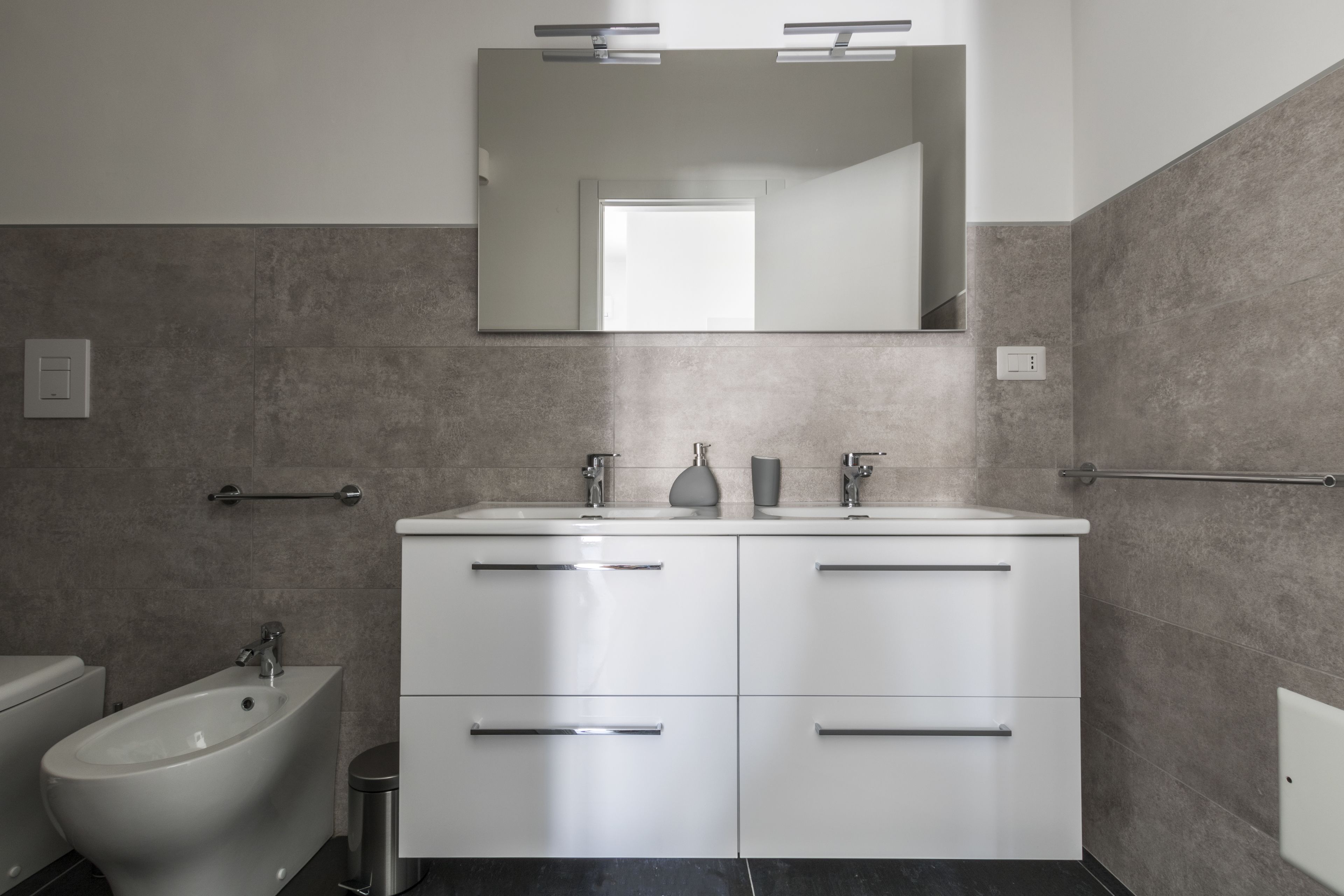 A modern bathroom with a bidet, double sinks, and a large mirror.