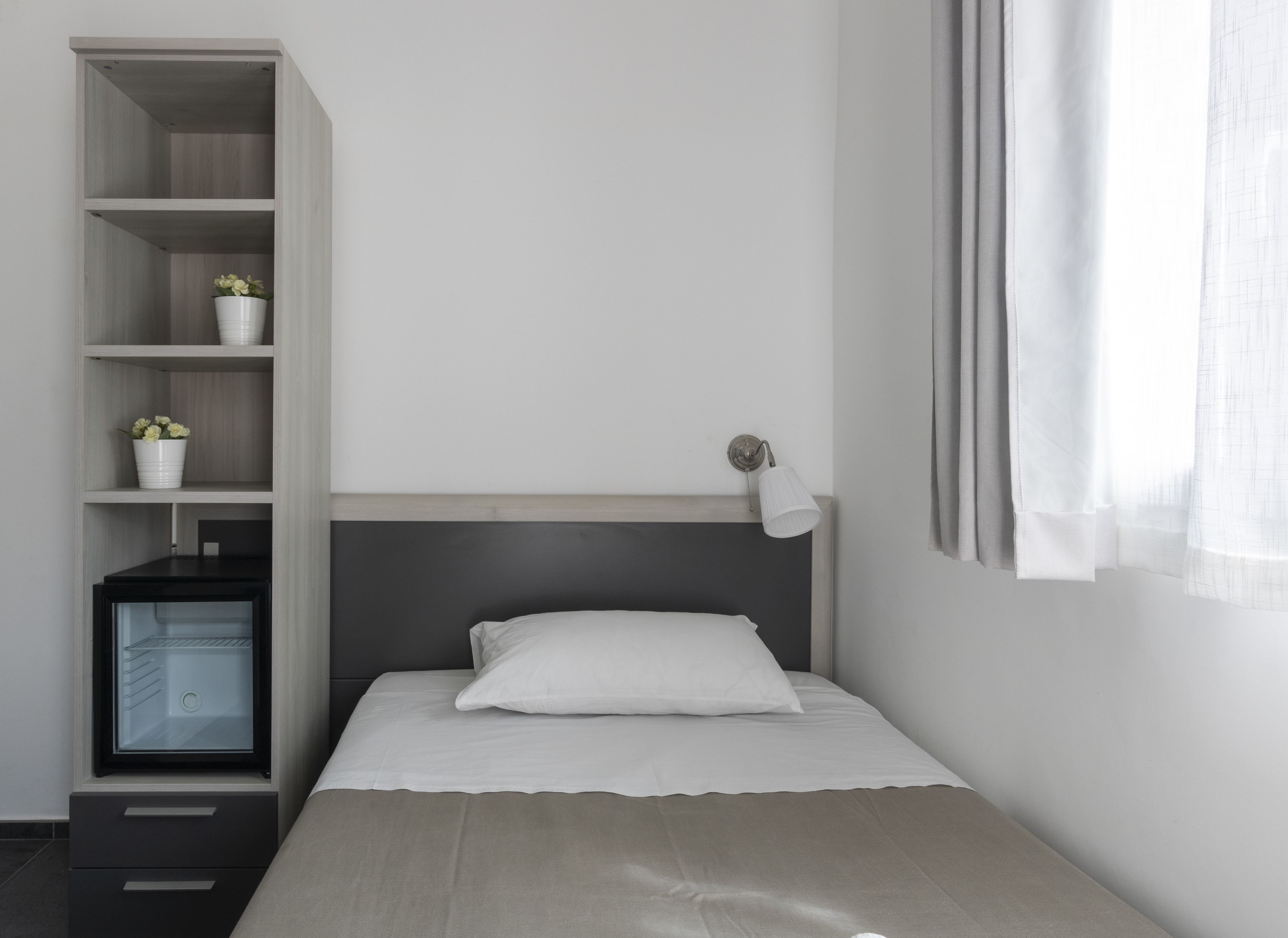 A bedroom with a bed, a nightstand, a built-in wardrobe, and a small desk with a lamp.