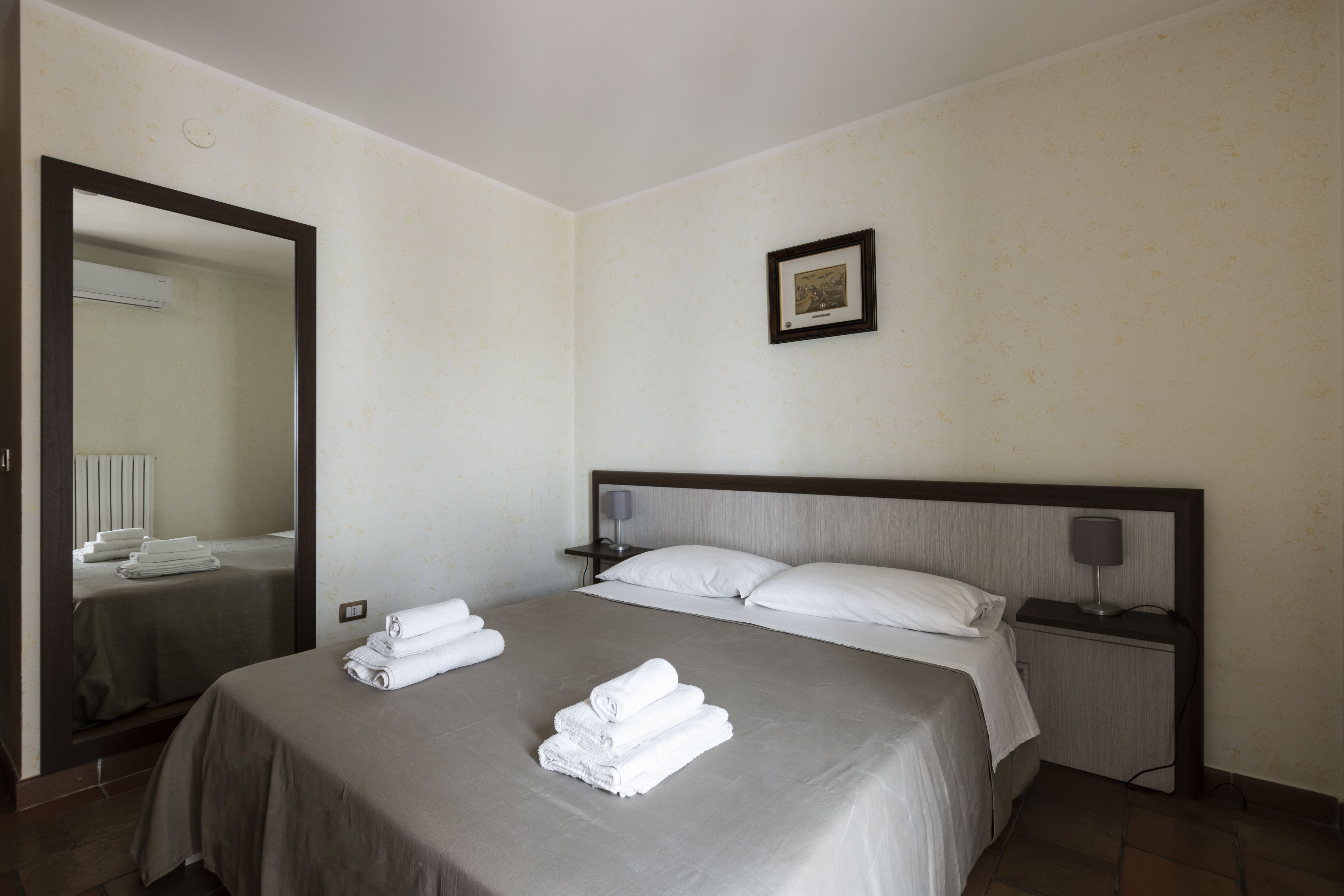 A neatly made bed with white linens and towels, a bedside table with a lamp, and a framed picture on the wall.