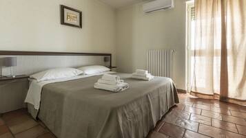 Habitación de hotel con cama, mesita de noche, lámpara, un cuadro en la pared y ventana con cortinas.