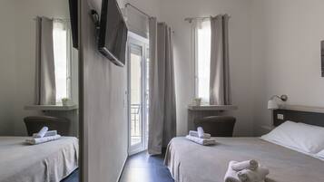 A hotel room with two beds, a TV mounted on the wall, and a balcony with curtains.