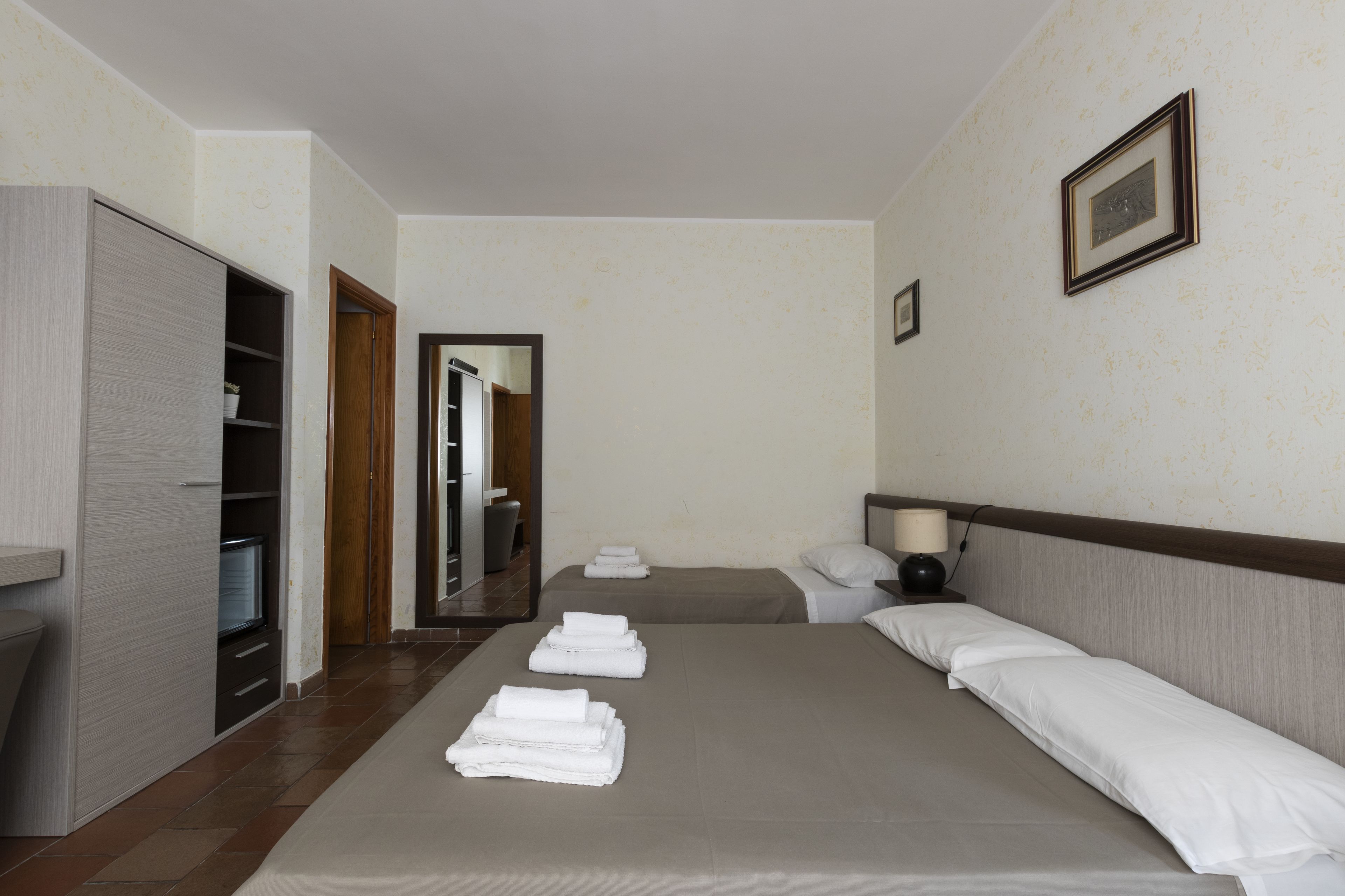 Habitación de hotel con una cama grande, un armario, un espejo y un cuadro enmarcado en la pared.