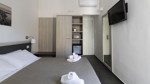 Een hotelkamer met een bed, een aan de muur bevestigde televisie, een magnetron en een klein kastje.