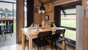 Un interior de madera con una mesa de comedor dispuesta para cuatro personas, sillas negras, una lámpara colgante y vistas al exterior.