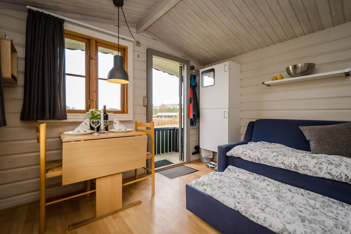 A cozy room with a wooden dining table, a blue sofa, and a small kitchen area with a fridge and shelf.