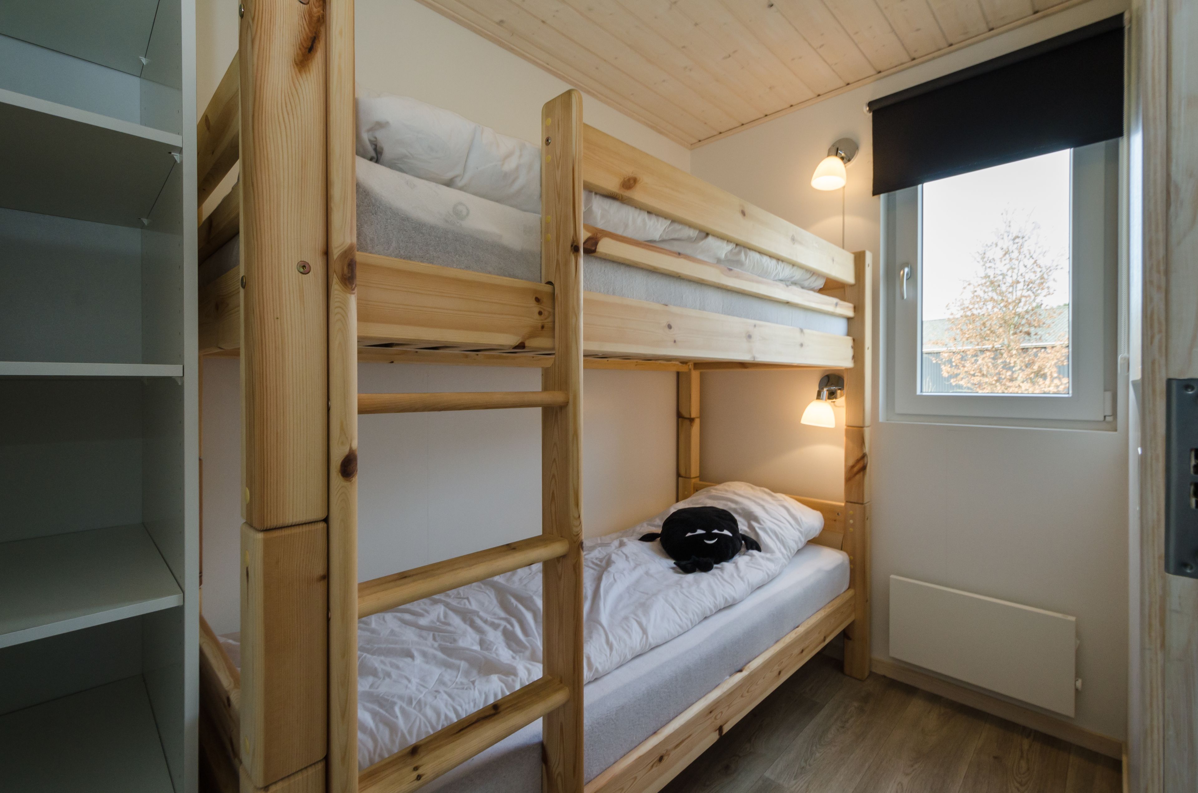 A bunk bed room with a window, a radiator, and a shelf unit.