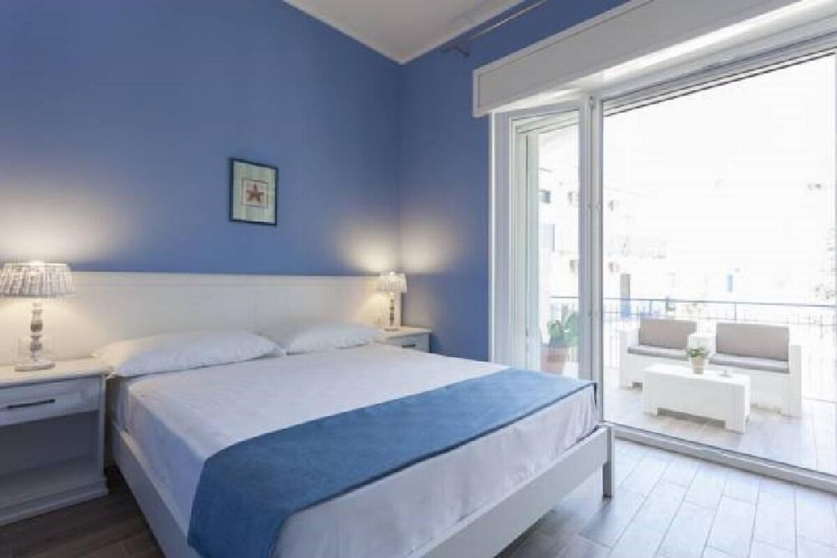 Ein Schlafzimmer mit einem großen Bett, einem Nachttisch, einer Lampe und Blick auf den Balkon.