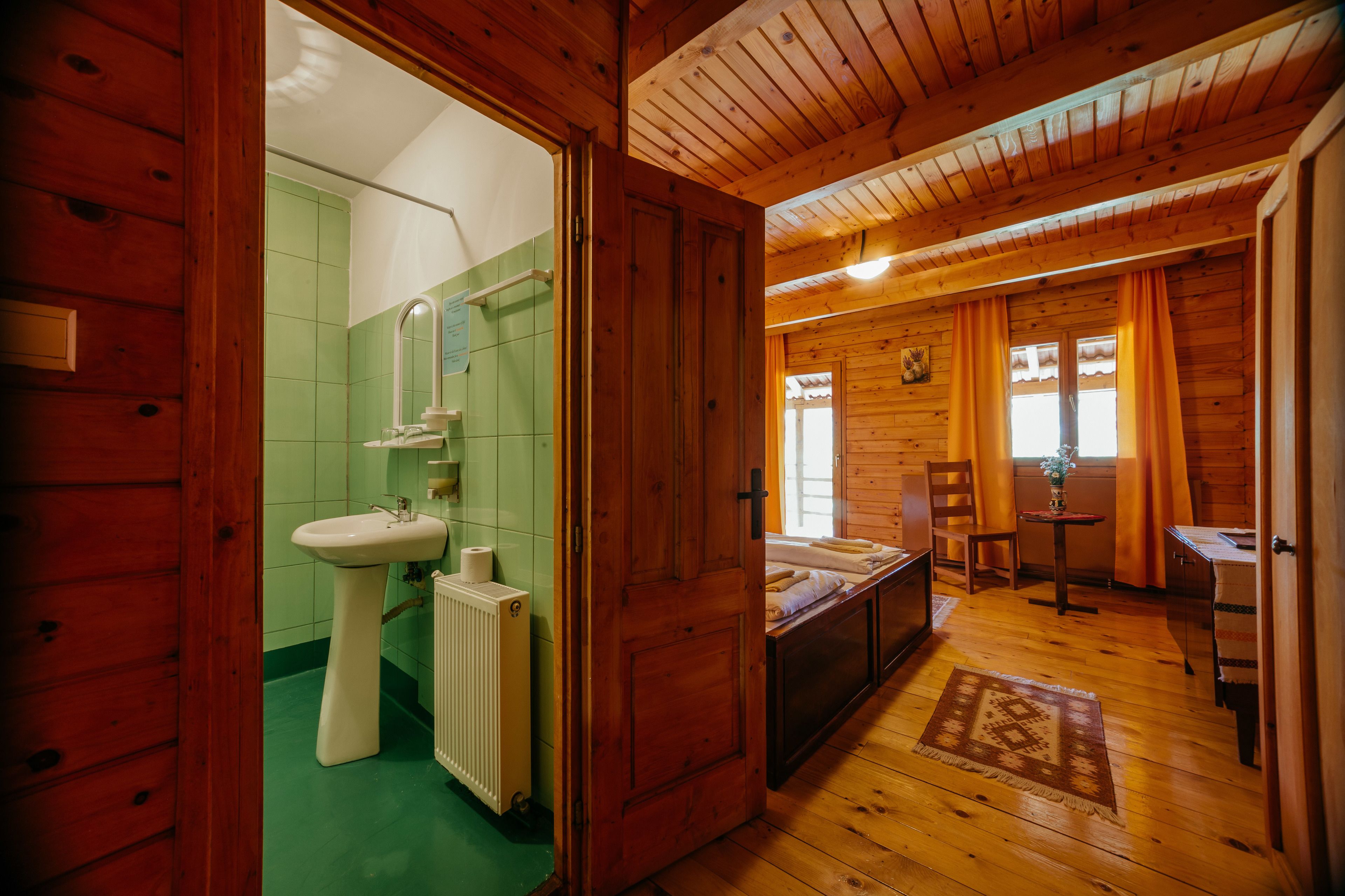 A wooden cabin interior with a bathroom, a bed, and a small table.