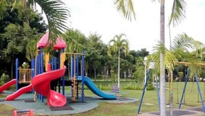 A playground with slides and swings, surrounded by grass and palm trees. - KK City HomeSuite at KK City Center 2 (Kota Kinabalu)