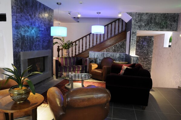 A modern living room with a fireplace, leather sofas, a glass coffee table, and a staircase with wooden railings. - Logis La Belle Meuniere (Royat)