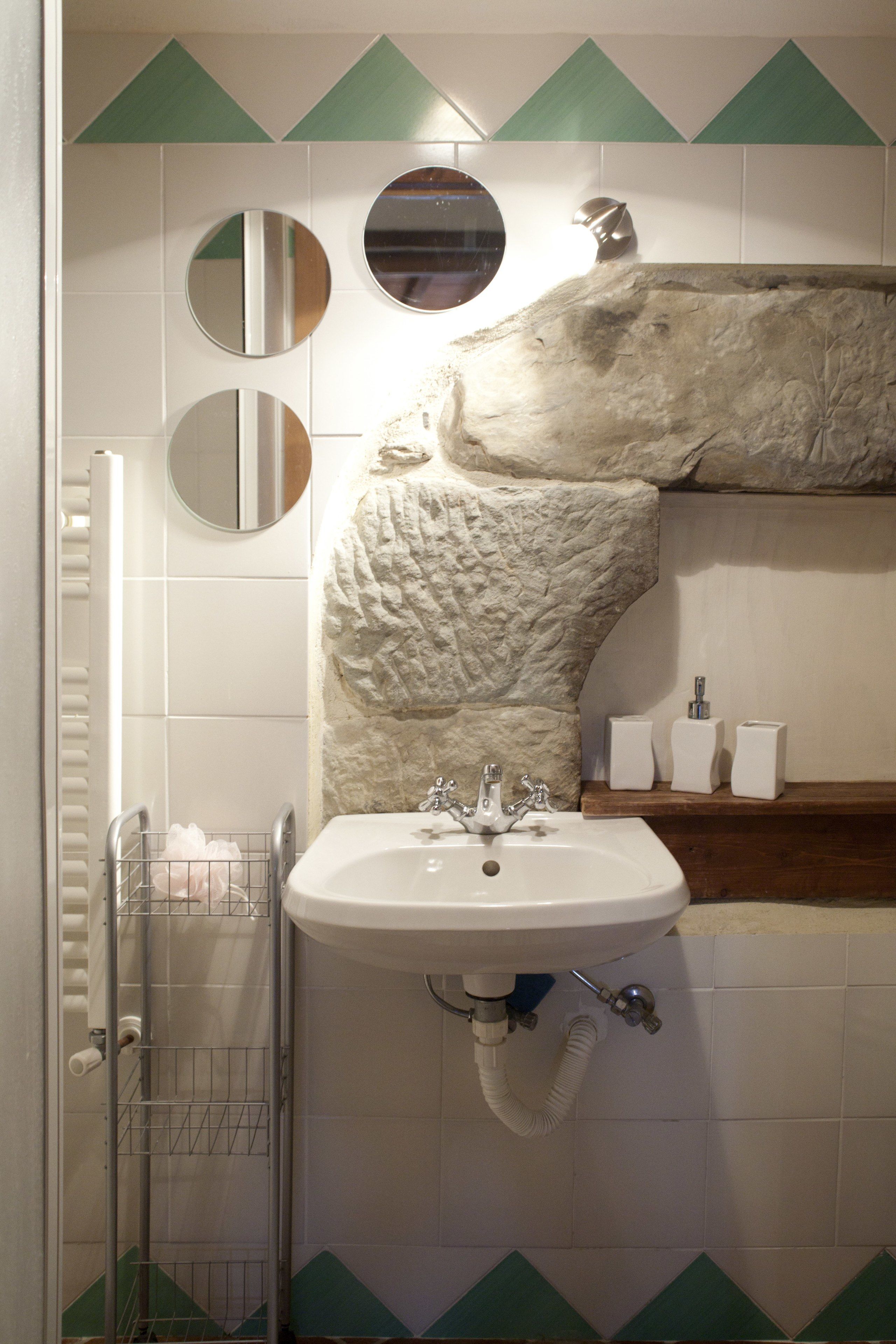 A bathroom with a sink, mirrors, a towel rack, and a decorative stone wall.