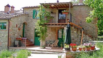 Una casa in pietra con un balcone, una scala in legno e vasi con piante.