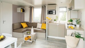 A modern living room with a sofa, a dining table, and a kitchen area with a microwave and sink. - Camping Le Marqueval (Hautot-sur-Mer)