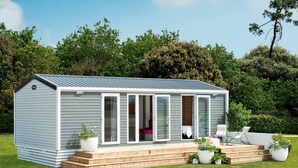 A small, single-story wooden structure with a sloped roof, large glass doors, and a small deck area with seating. - Camping Le Marqueval (Hautot-sur-Mer)