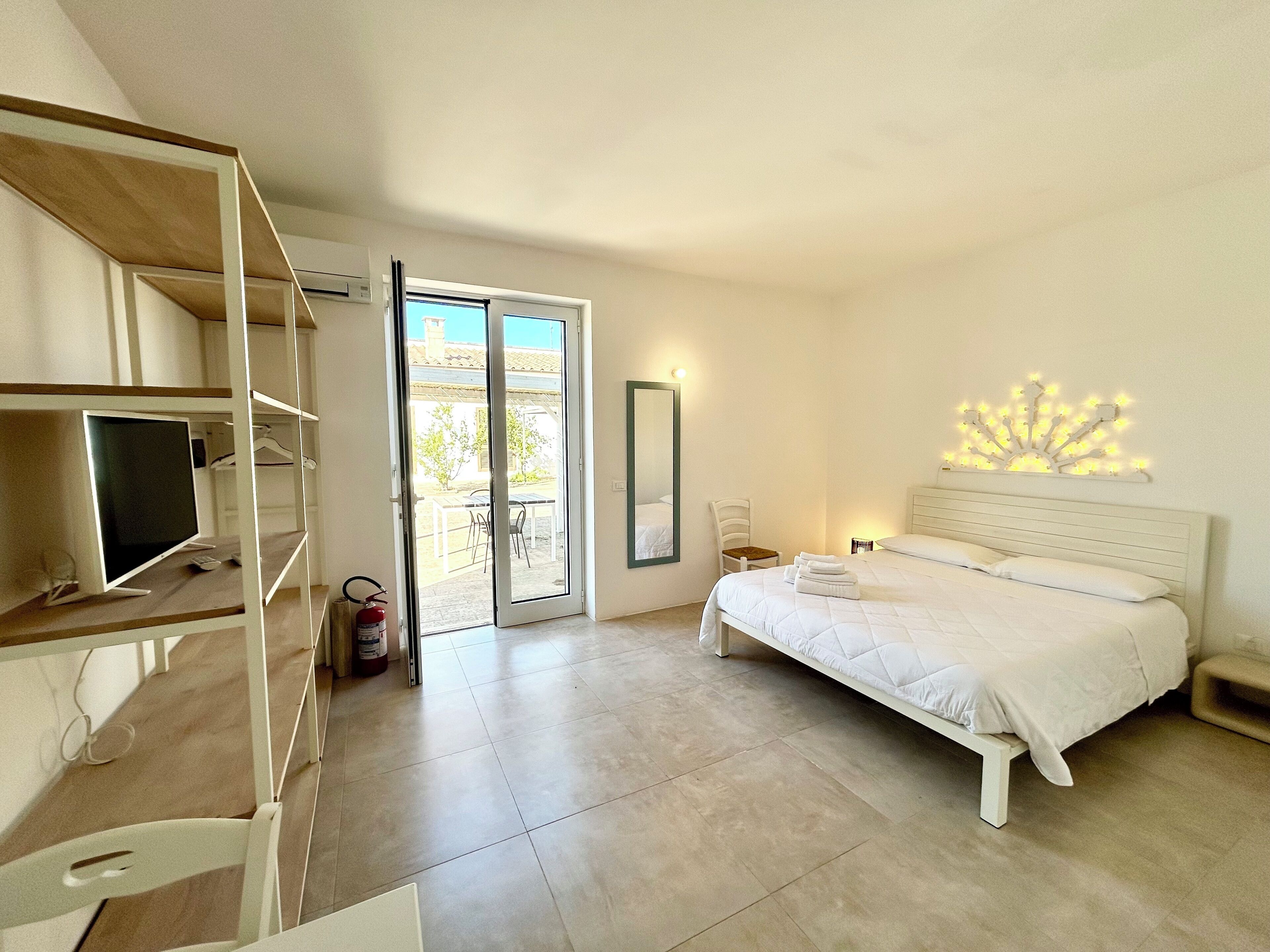 Une chambre avec un lit, un bureau avec un ordinateur, une chaise, une table de chevet, un miroir et un balcon avec vue.