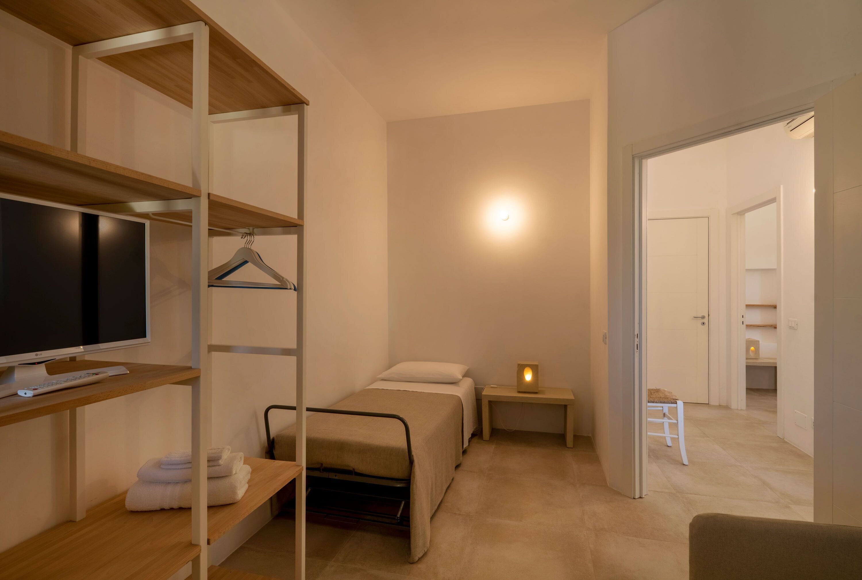 A bedroom with a bed, a TV, a bedside table with a lamp, and a hanging clothes rack.