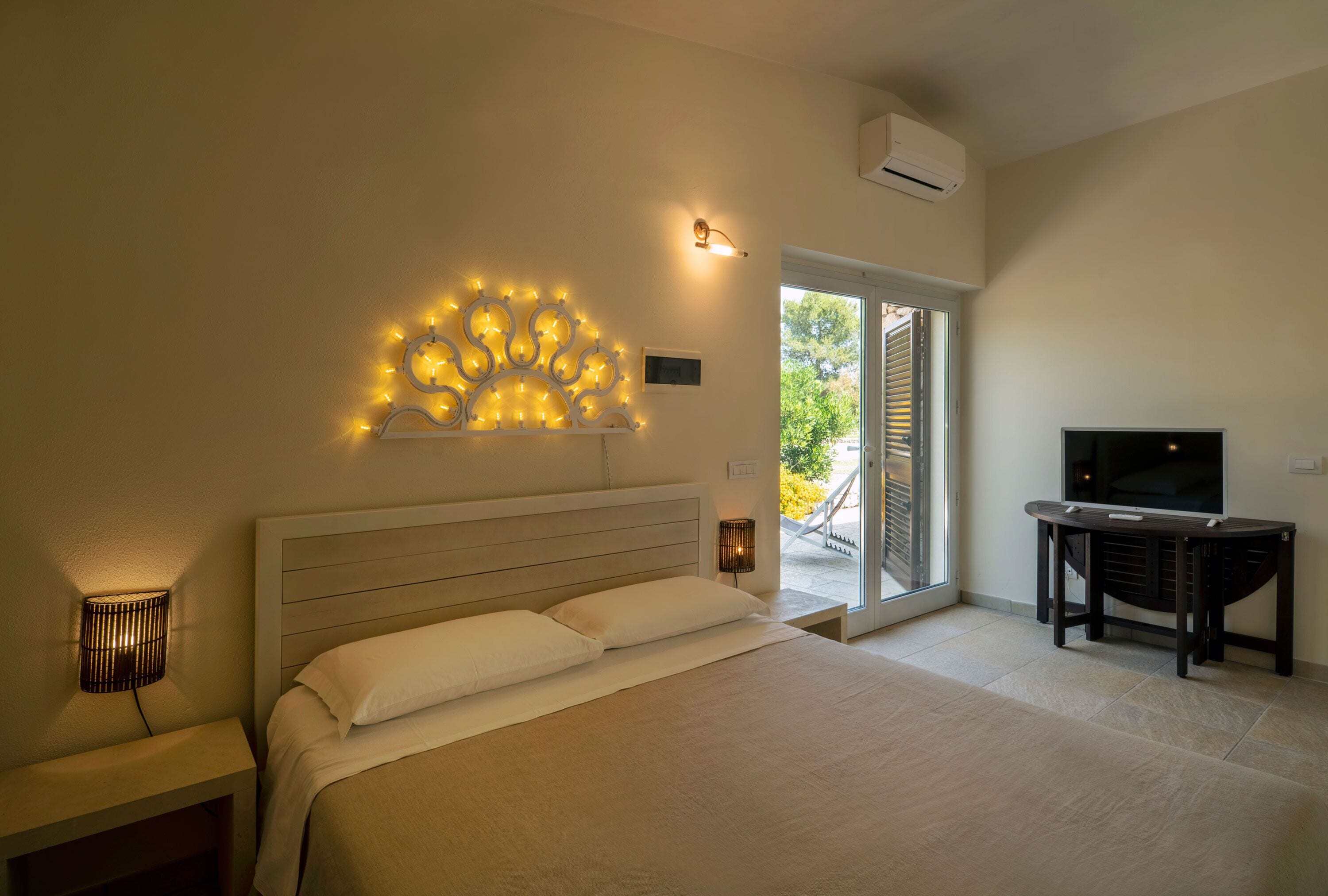 Ein Schlafzimmer mit Bett, Nachttischlampen, einem Fernseher und einem Balkon mit Blick.