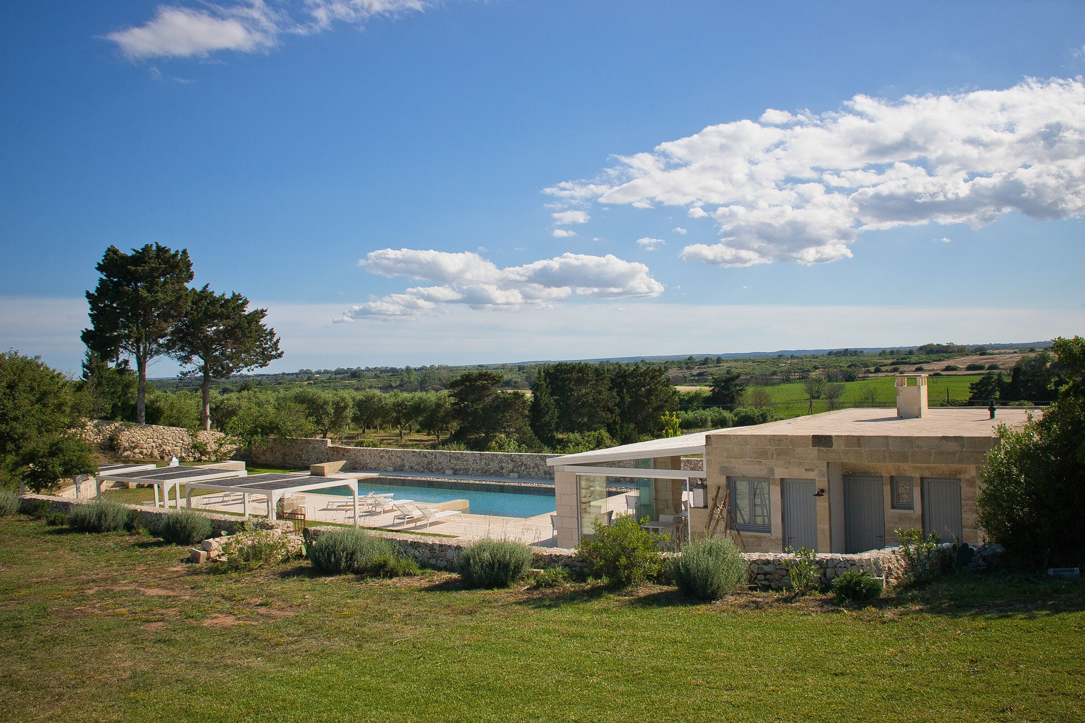 Una casa moderna con piscina, rodeada de vegetación y un cielo despejado.