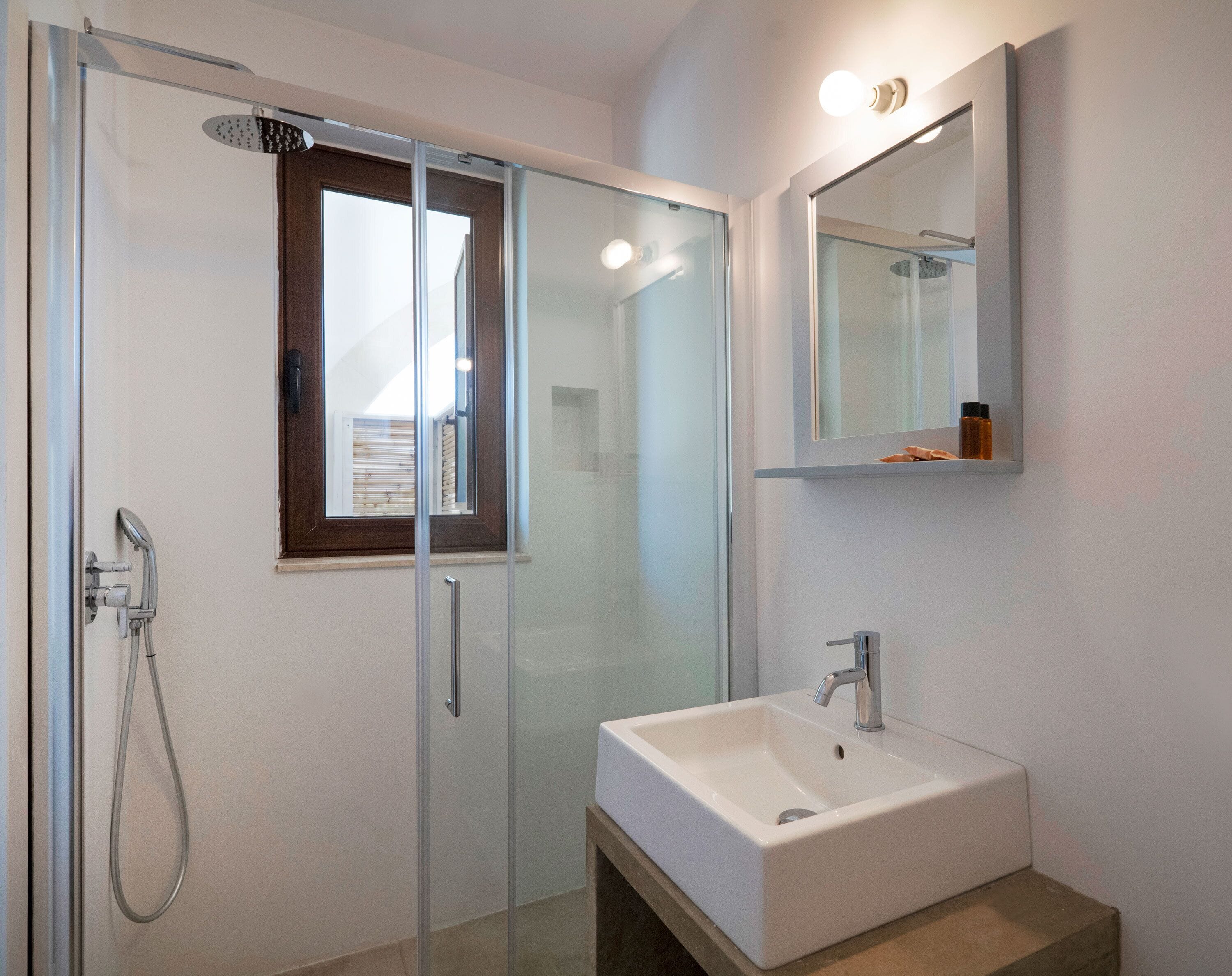 Ein modernes Badezimmer mit einer Duschkabine aus Glas, einem weißen Waschbecken und einem Spiegel darüber.