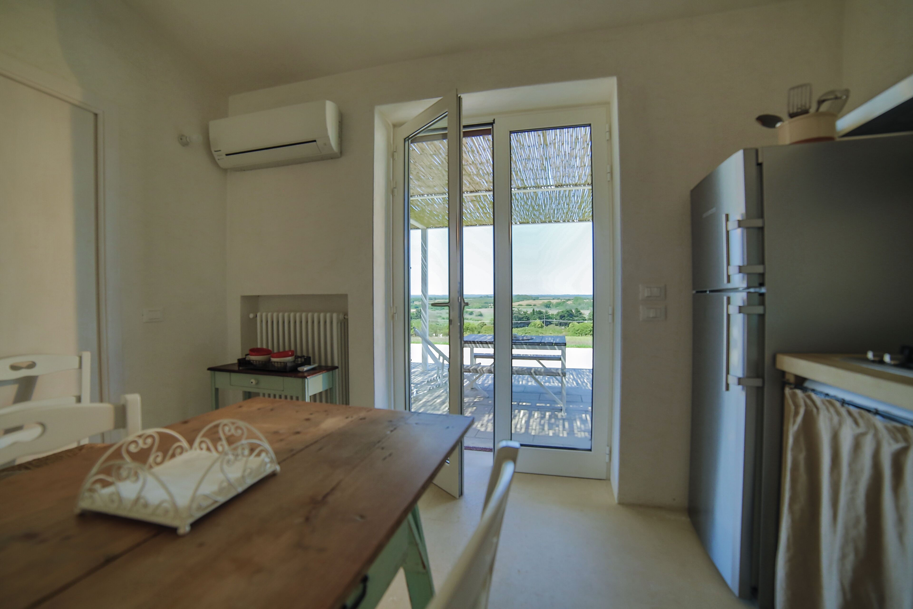 A compact kitchen with a wooden table, a refrigerator, and a sliding glass door leading to an outdoor area.