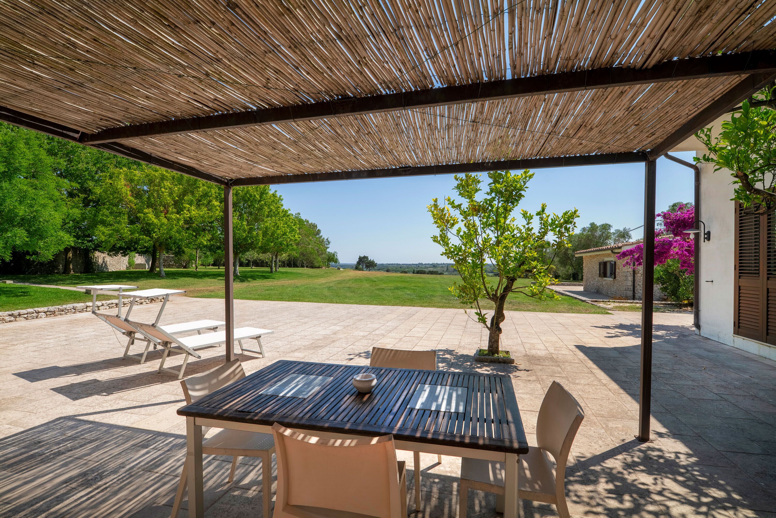 An outdoor patio with a table and chairs, a pergola, and a view of a green landscape.