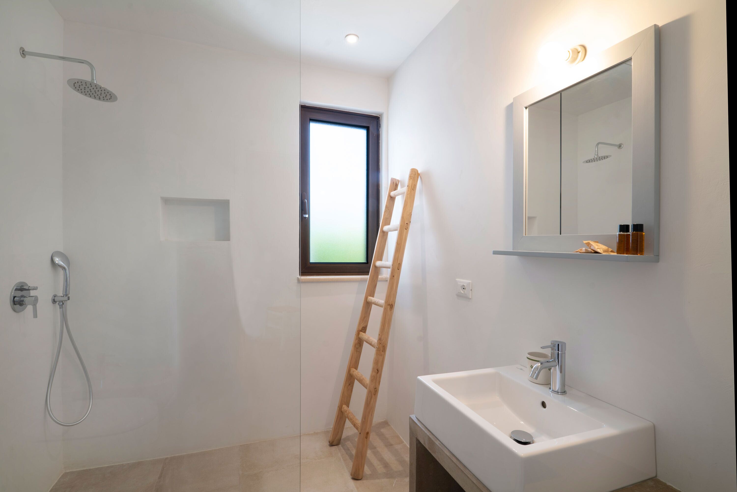 Een moderne badkamer met een douche, een wastafel, een spiegel en een houten ladder die tegen de muur staat.