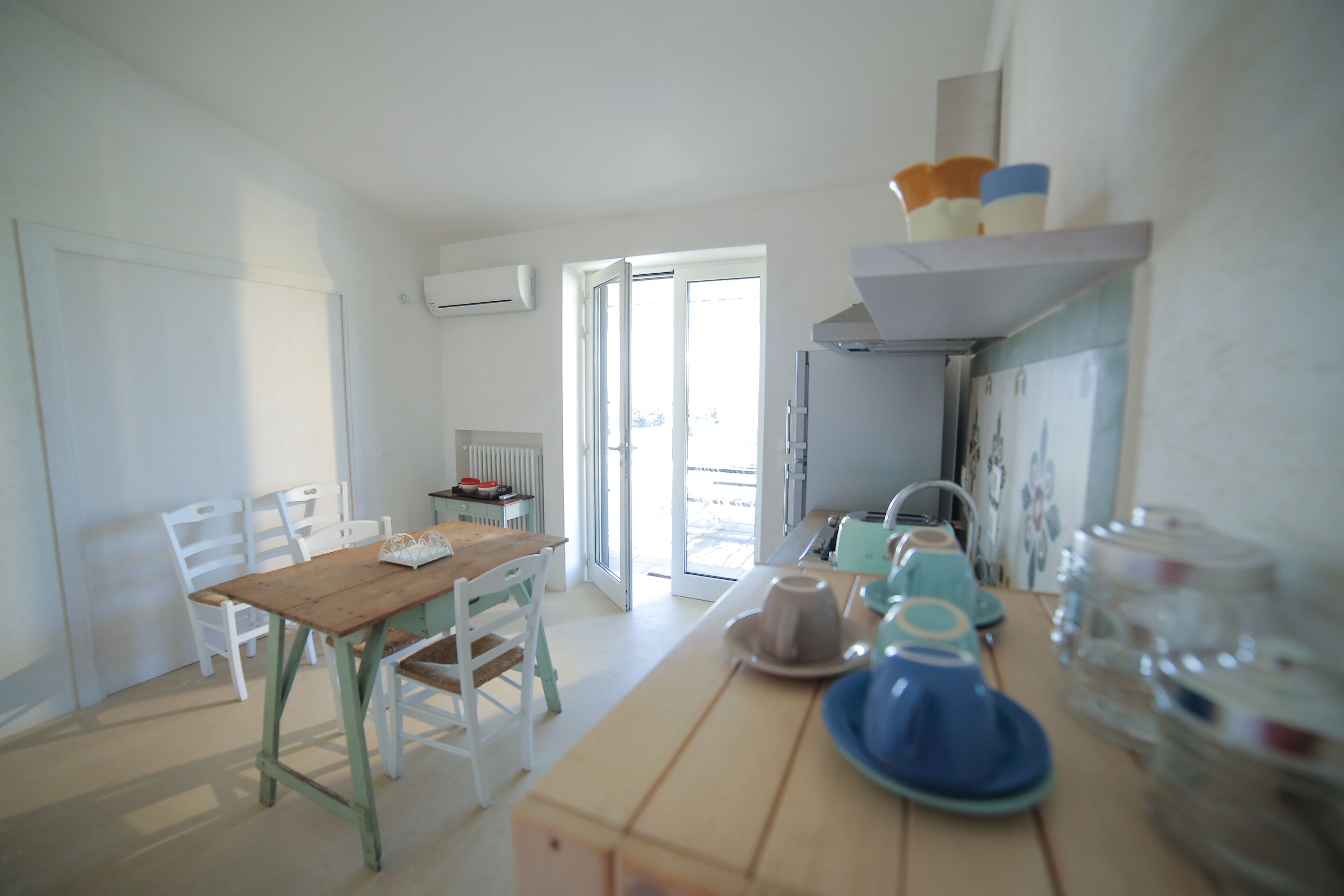 A bright kitchen with a wooden table, white chairs, and a window.
