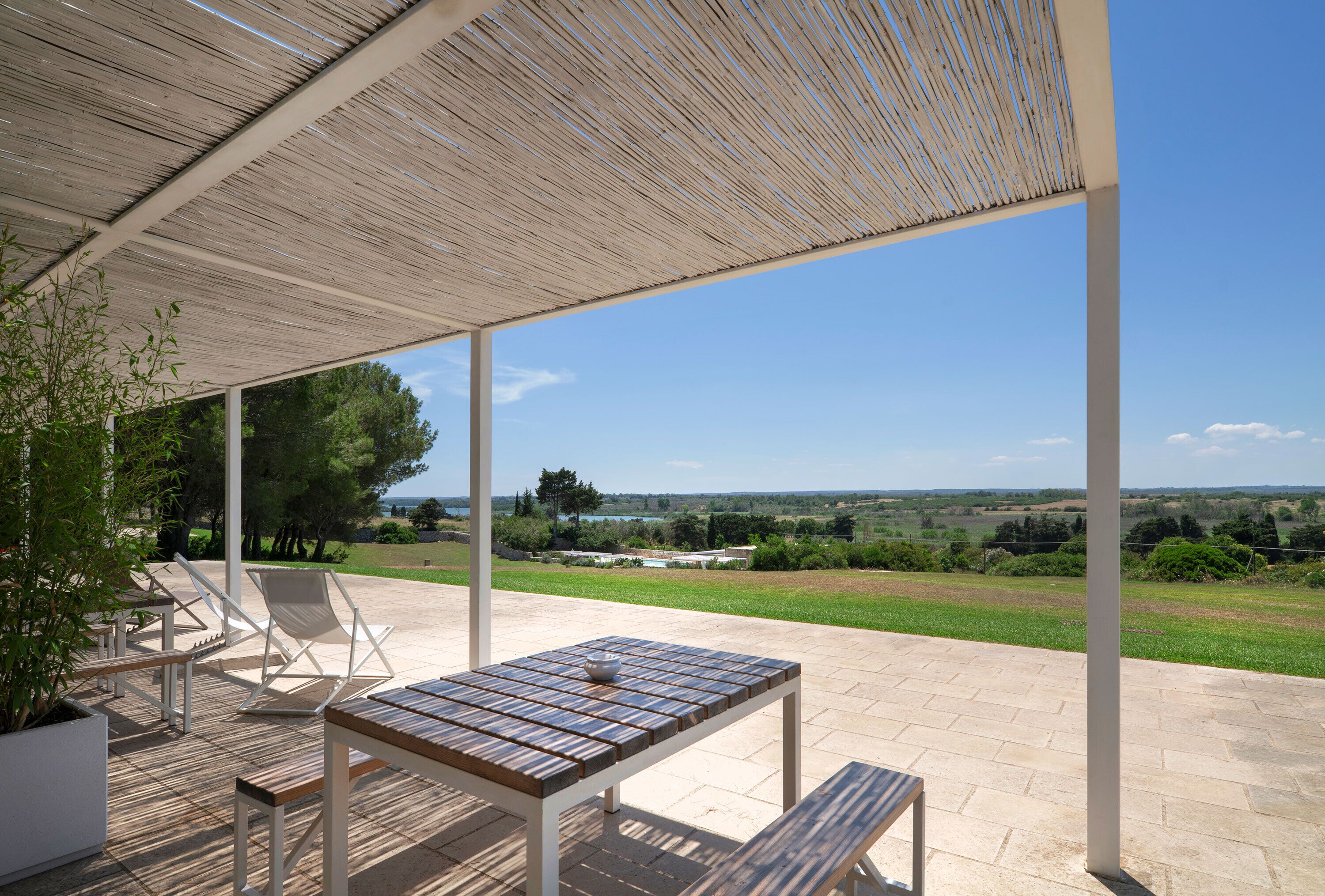 Une terrasse extérieure avec une table et des chaises, une pergola et une vue panoramique sur la campagne.