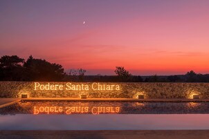 A stone wall with illuminated text reading "Podere Santa Chiara" and "Bottega 21 Chiara".
