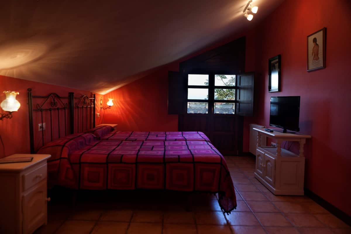 Ein Schlafzimmer mit Bett, Schminktisch, Fernseher und einem Fenster mit Vorhängen.