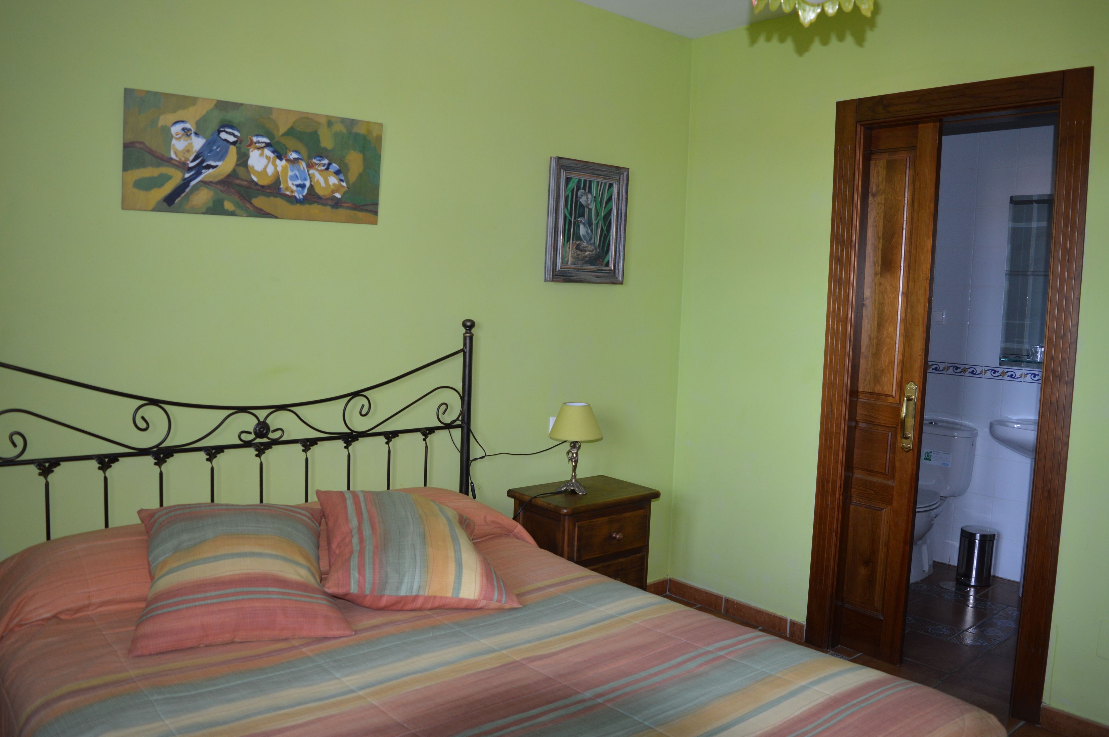 A bedroom with a bed, a nightstand, a lamp, and a door leading to a bathroom.