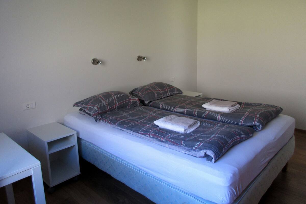 Un lit double avec une couette à carreaux, une petite table de chevet et une commode.