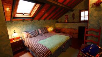 Un dormitorio acogedor con techo inclinado, tragaluz, cama con ropa de cama a cuadros, mesita de noche con lámpara y cómoda.