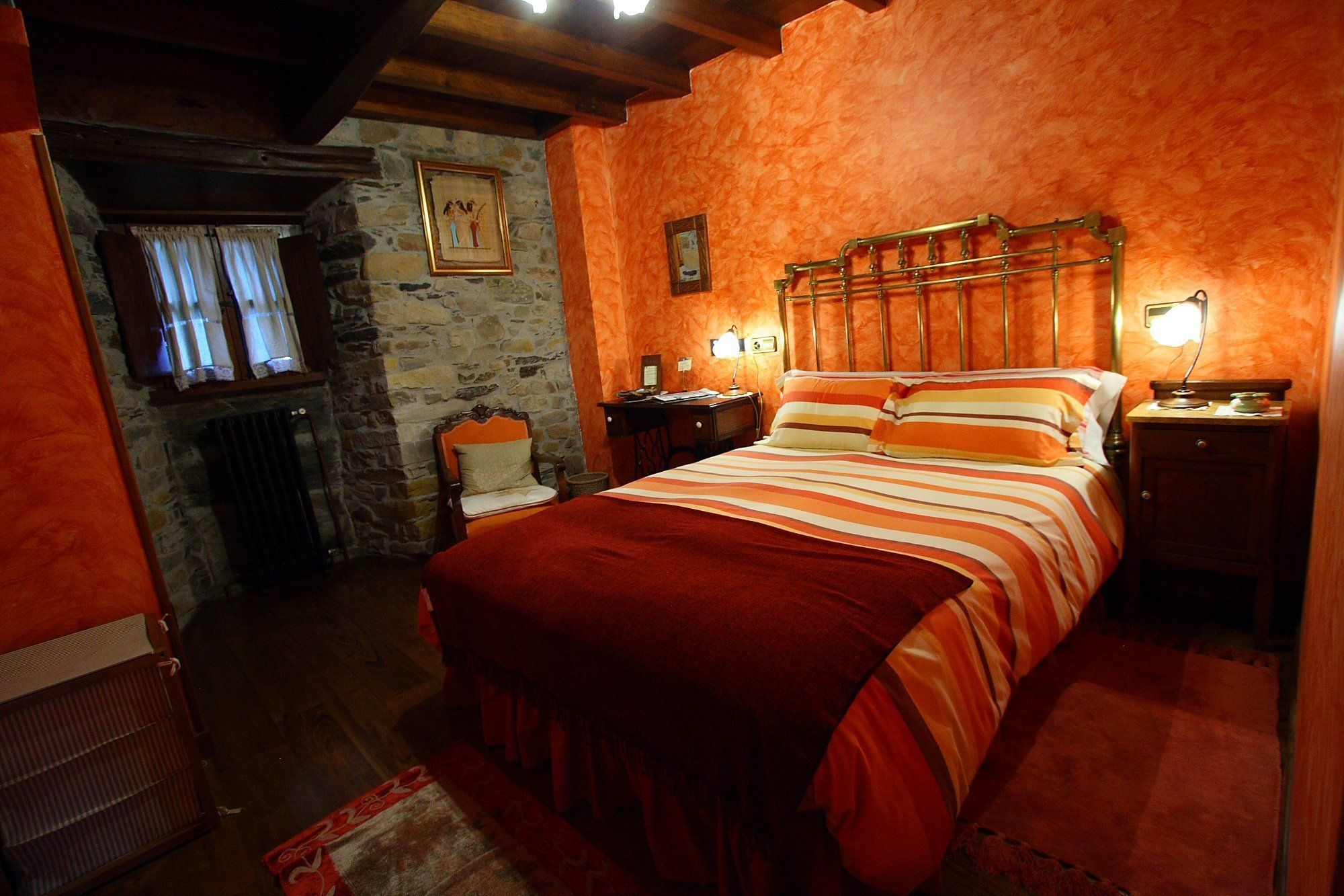 A cozy room with a bed, a desk, and a chair. There is a stone wall and a wooden ceiling.