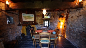 A rustic dining area with a stone wall, wooden table, and chairs. A map is displayed on the wall, and a fireplace is visible in the background. - Casa La Fonte (Valdes)