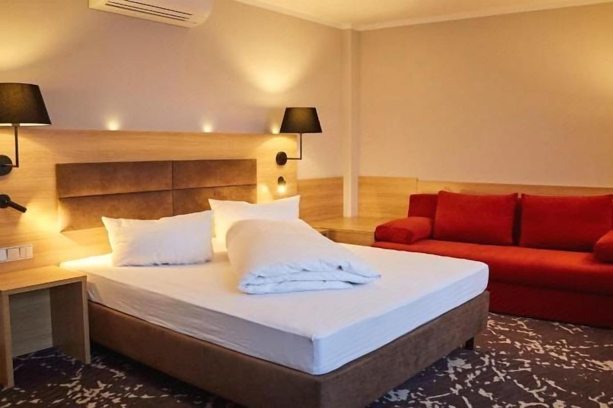 A hotel room with a bed, two bedside tables, a red sofa, and a carpeted floor.