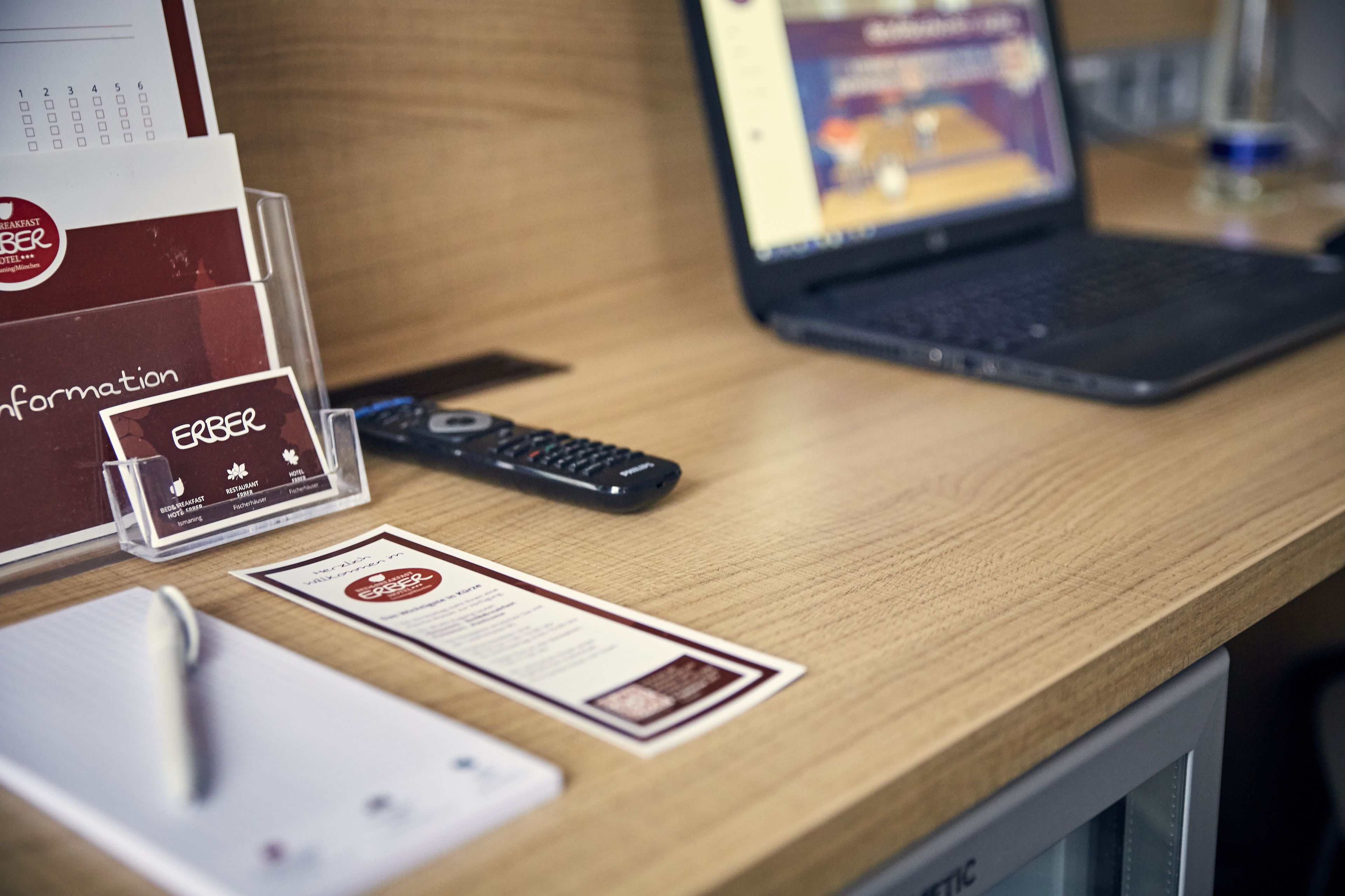 A hotel reception desk with a laptop, a remote control, a pen, and a brochure.