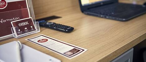 A hotel reception desk with a laptop, a remote control, a pen, and a brochure.