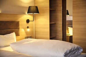 Une chambre d’hôtel avec un lit bien fait, une lampe fixée au mur et une tête de lit en bois.