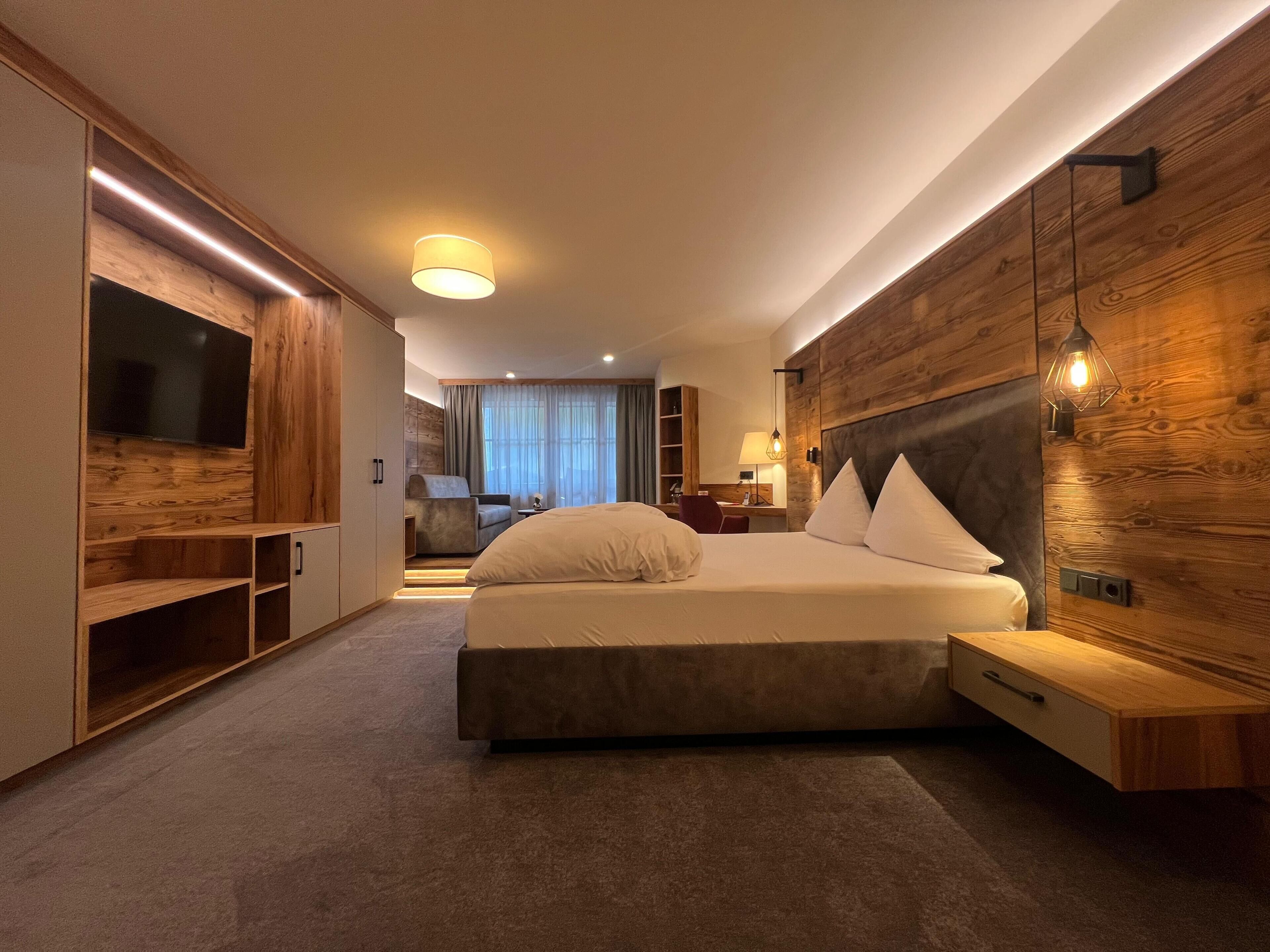 Ein modernes Hotelzimmer mit einem großen Bett, Holzvertäfelung, einem Fernseher und einem Schreibtisch.